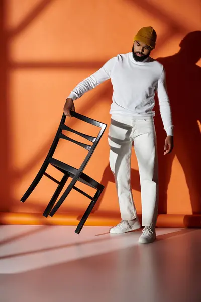 Schöner Mann in modischer Kleidung mit Stuhl vor lebhafter orangefarbener Wand. — Stockfoto