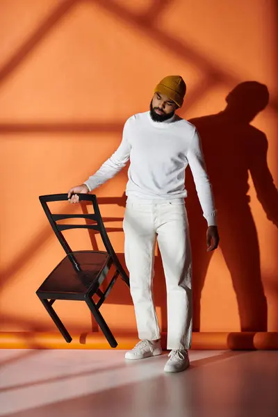 Handsome African American man in fashionable attire standing thoughtfully next to a chair in a vibrant room. — Stock Photo