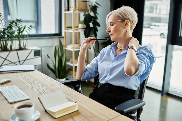 A middle aged businesswoman with short hair concentrates on work at her desk in the office during menopause. — Stock Photo