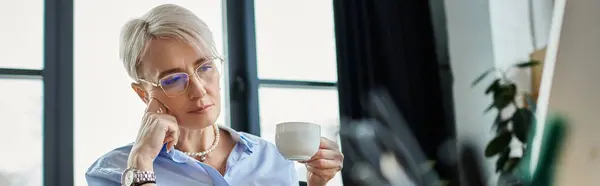 Una mujer de negocios de mediana edad con el pelo corto en una camisa azul sosteniendo pacíficamente una taza. - foto de stock