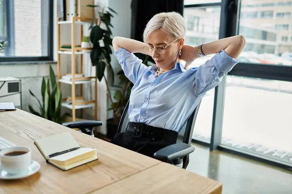 Middle-aged businesswoman with short hair sitting at desk, hands behind head, deep in thought and contemplation. — Stock Photo