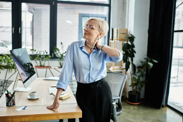 A middle aged businesswoman with short hair working diligently at a desk, feeling unwell during menopause. — Stock Photo