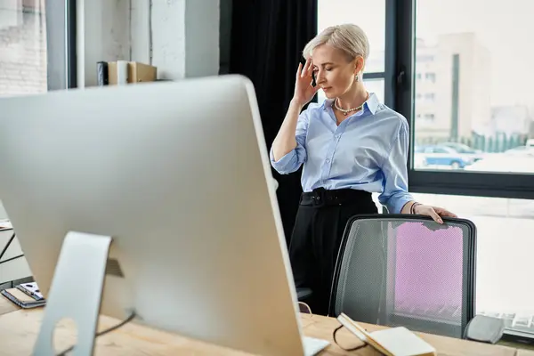 Femme d'affaires d'âge moyen avec les cheveux courts travaillant sur un ordinateur dans un bureau, se sentant mal pendant la ménopause — Photo de stock