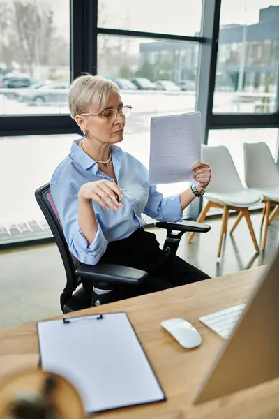 A middle-aged businesswoman with short hair deeply engrossed in reading a piece of paper at her office desk. — Stock Photo