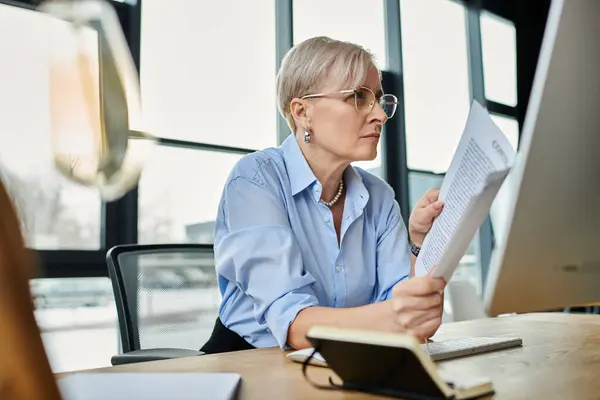 Middle-aged businesswoman with short hair engrossed in reading while working in her office — Stock Photo