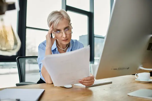 Femme d'affaires d'âge moyen aux cheveux courts se concentrant sur son écran d'ordinateur tout en travaillant au bureau. — Photo de stock