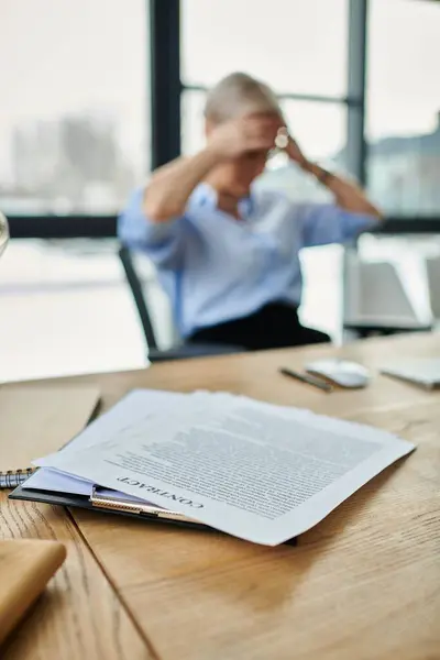 Middle-aged woman sits at table with book and pen, deep in thought. — Stock Photo