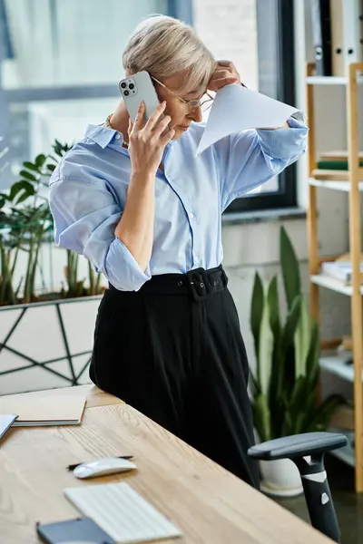A middle aged businesswoman with short hair, during menopause, stands in an office engaged in negotiations on a cell phone. — Stock Photo