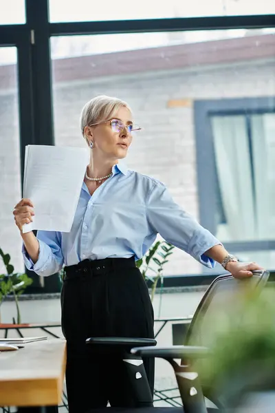 Middle-aged businesswoman with short hair stands confidently in office, holding piece of paper while working diligently. — Stock Photo