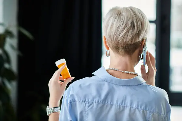 Femme d'affaires d'âge moyen avec les cheveux courts parlant sur le téléphone portable, tenant bouteille avec des médicaments — Photo de stock