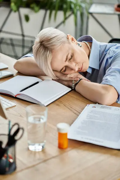 Middle-aged businesswoman with short hair is resting her head on her hands at a table, overwhelmed during menopause in the office. — Stock Photo