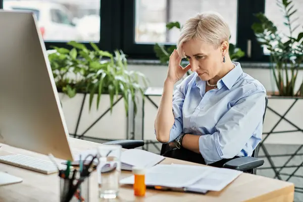 Middle-aged businesswoman with short hair works diligently at her desk in front of a computer during menopause. — Stock Photo