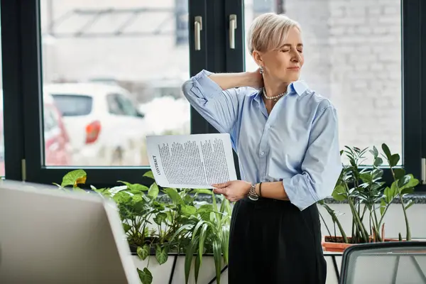Middle-aged businesswoman with short hair standing in front of a computer, feeling unwell — Stock Photo