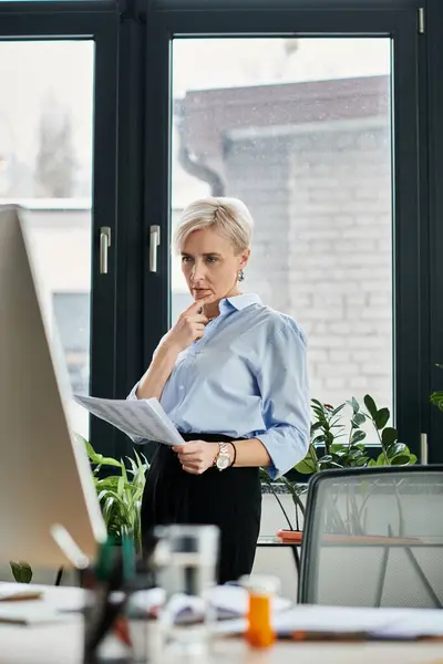A middle-aged businesswoman with short hair stands in front of a computer, intensely focused on her work — Stock Photo