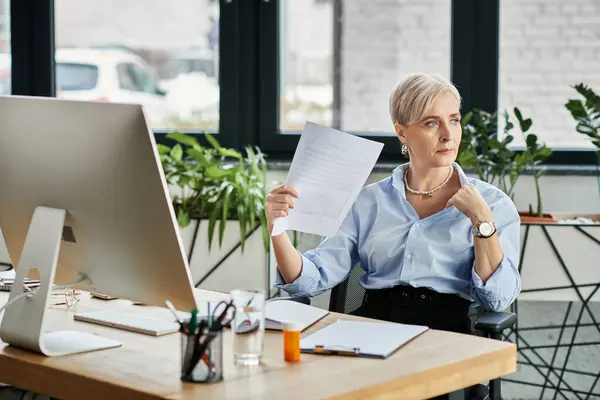 Middle-aged businesswoman with short hair sitting at a desk, deep in thought while holding a piece of paper. — Stock Photo