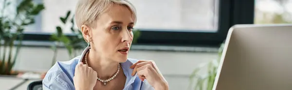A middle-aged businesswoman with short hair focuses intently on her laptop screen while working in an office setting. — Stock Photo