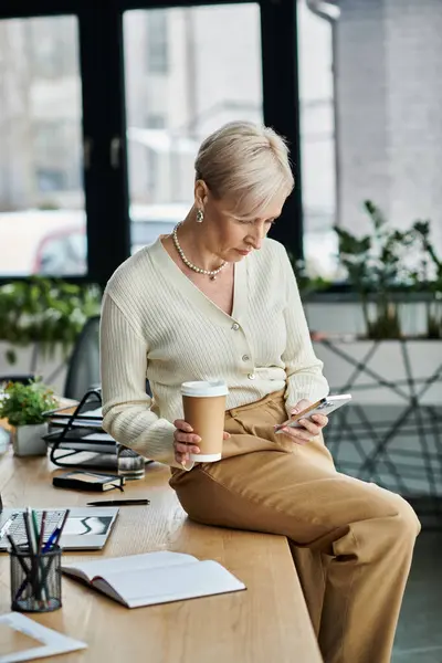 Middle-aged businesswoman with short hair enjoys a moment of relaxation, sipping coffee at a modern office. — Stock Photo