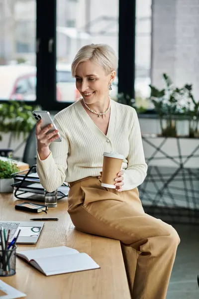 Middle-aged businesswoman with short hair sitting at a table, savoring a cup of coffee in a modern office. — Stock Photo