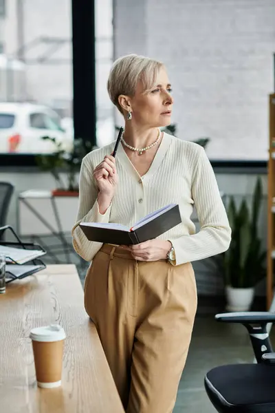 Geschäftsfrau mittleren Alters steht in einem modernen Büro und hält ein Buch. — Stockfoto