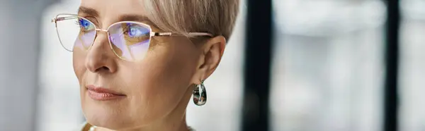 A middle-aged businesswoman with short hair wearing glasses gazes thoughtfully to the side in a modern office setting. — Stock Photo