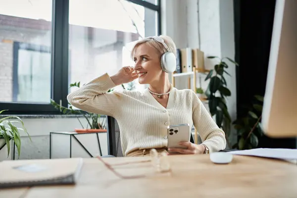 A middle-aged businesswoman with short hair sitting at a desk, actively using a cell phone for work. — Stock Photo