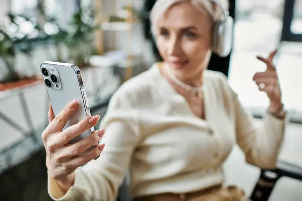 Eine Geschäftsfrau mittleren Alters mit kurzen Haaren benutzt ein Mobiltelefon in einem modernen Büroumfeld. — Stockfoto