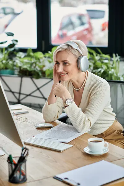 A middle-aged businesswoman with short hair sits at a table, focused on her laptop and wearing headphones. — Stock Photo