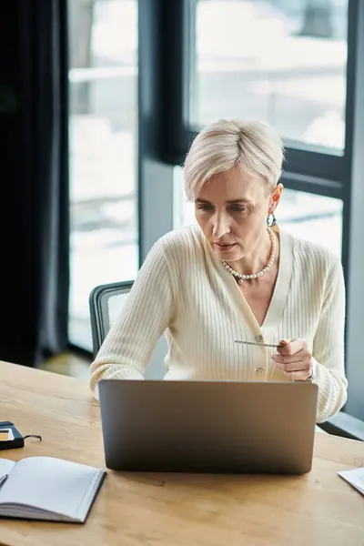 A middle-aged businesswoman with short hair sits in a modern office, engrossed in her work on a laptop computer. — Stock Photo