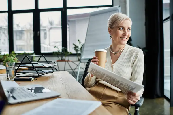 Uma empresária de meia-idade com cabelo curto senta-se em uma cadeira, segurando serenamente uma xícara de café em um ambiente de escritório moderno. — Fotografia de Stock