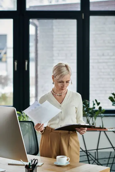 Businesswoman stands with laptop and paper in modern office. — Stock Photo