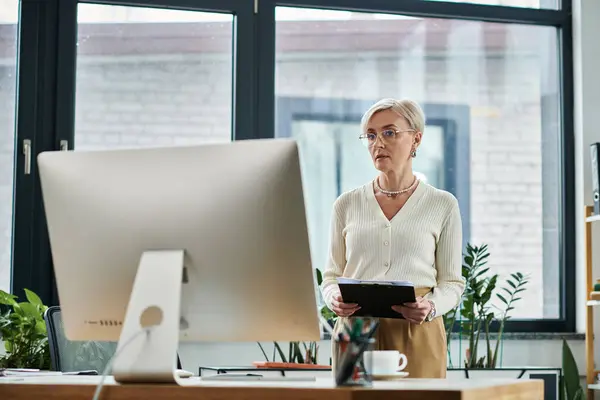 Geschäftsfrau mittleren Alters mit kurzen Haaren navigiert gekonnt am Computer im eleganten modernen Büro. — Stockfoto