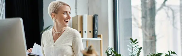 Geschäftsfrau mittleren Alters mit kurzen Haaren steht selbstbewusst vor einem Laptop in einem modernen Büroambiente. — Stockfoto