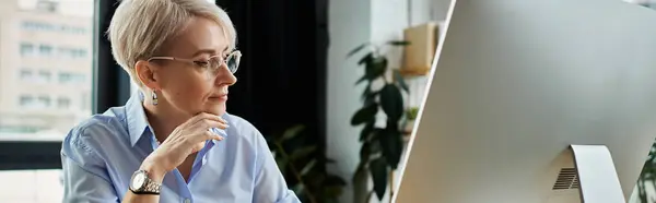 A middle-aged businesswoman with short hair works at her desk, focused on the computer screen in her office — Stock Photo