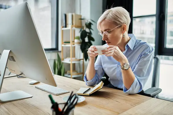 A focused middle-aged businesswoman with short hair sips coffee while deep in thought at her desk — Stock Photo
