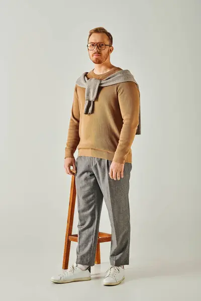 A stylish man poses on a stool with a sweater elegantly draped around his neck. — Stock Photo