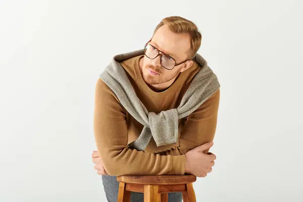 Handsome man in stylish attire, sitting on a stool with arms crossed in a confident pose. — Stock Photo