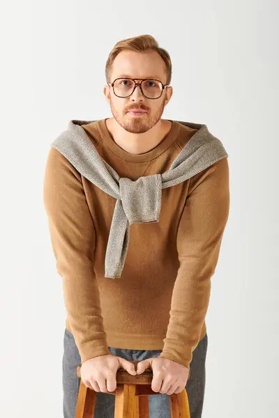 Handsome man in sweater and glasses poses on stool. — Stock Photo