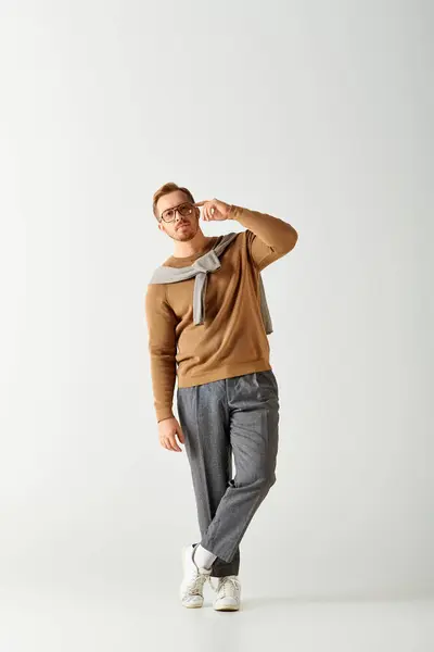 Un bell'uomo in un maglione marrone e pantaloni grigi colpisce una posa elegante. — Foto stock