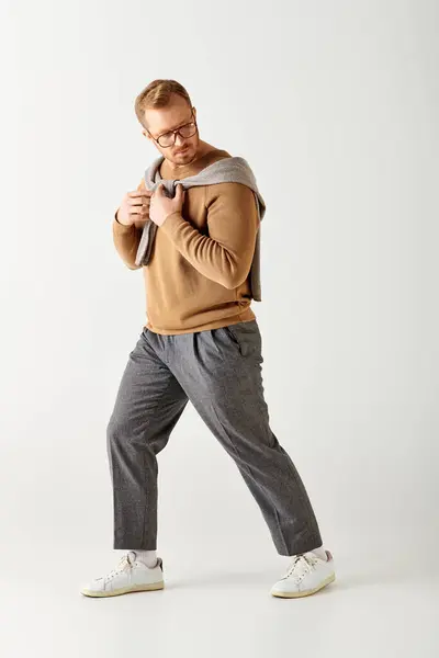 Uomo elegante in maglione marrone e pantaloni grigi colpisce una posa dinamica. — Foto stock