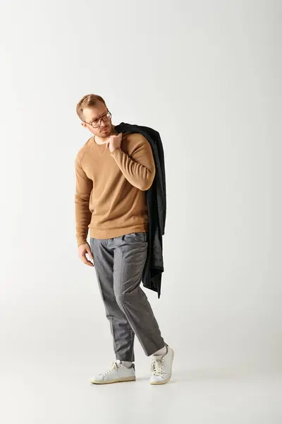 A handsome man poses confidently in a brown sweater and grey pants. — Stock Photo