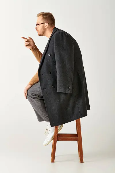 Stylish man sitting atop wooden stool with poise. — Stock Photo