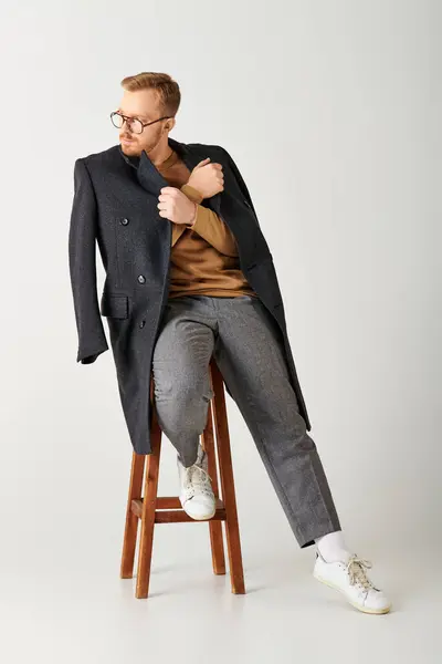 Handsome man in stylish attire, actively posing on a wooden stool. — Stock Photo