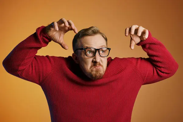 Schöner Mann im roten Pullover posiert mit den Händen über dem Kopf. — Stockfoto