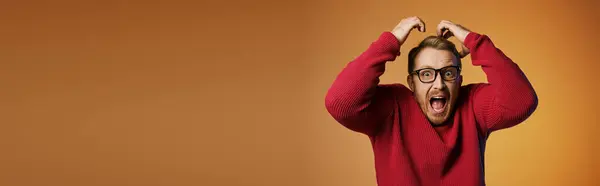 Handsome man in red sweater holding head with hands. — Stock Photo