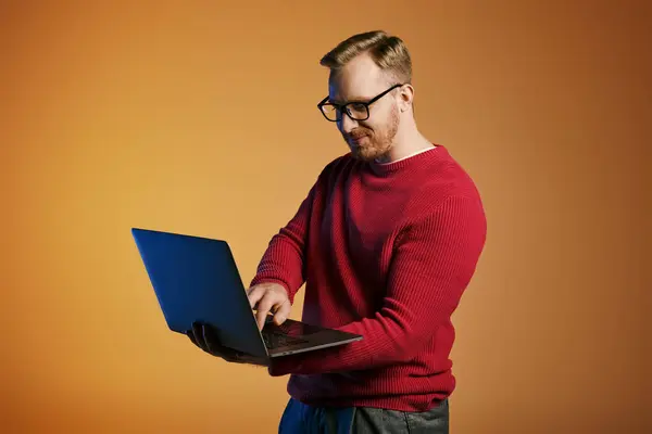 Stylish man in a red sweater actively using a laptop. — Stock Photo
