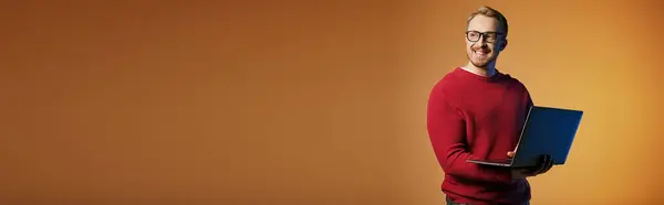 Stylish man in red sweater is holding a laptop. — Stock Photo
