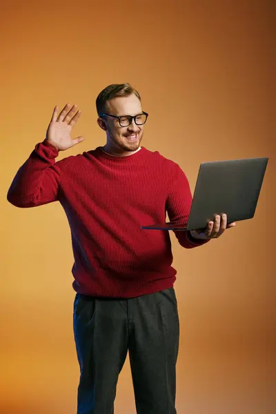 Ein zierlicher Mann im roten Pullover hält einen Laptop in der Hand. — Stockfoto