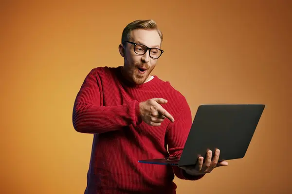 Beau homme dans un pull rouge pointe activement sur un ordinateur portable. — Photo de stock