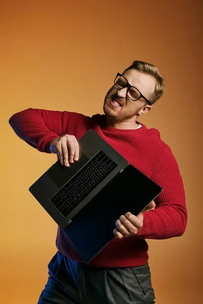 Handsome man in red sweater actively holding a laptop. — Stock Photo