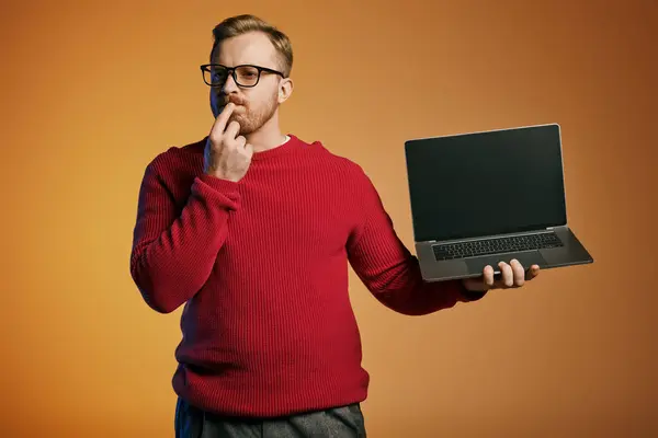 Un uomo alla moda con un maglione rosso in mano un computer portatile. — Foto stock